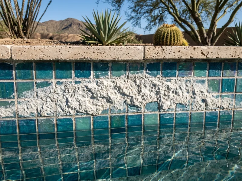 Chalky white calcium scale banded across glass waterline tile, with clean mosaic below.