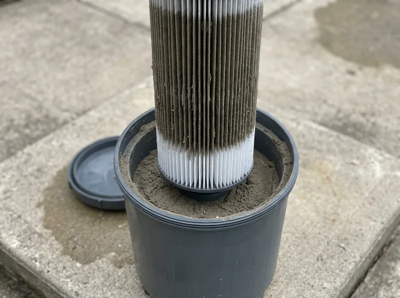 A pool filter cartridge lifted out of its housing, the pleats packed with grey debris.